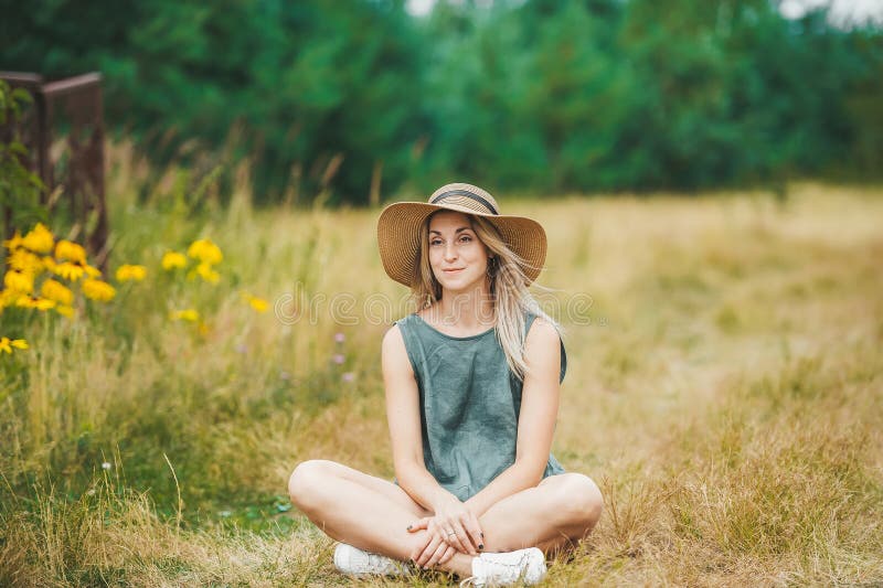 Le den unga kvinnan i hatt för att sitta i lotusblomma posera på sommarängen royaltyfri bild Le den unga kvinnan i hatt för att sitta i lotusblomma posera på sommarängen royaltyfri bild