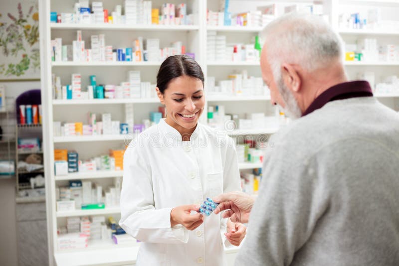 Le den unga kvinnliga apotekaren som ger receptläkarbehandlingpiller till den höga manliga patienten royaltyfri bild