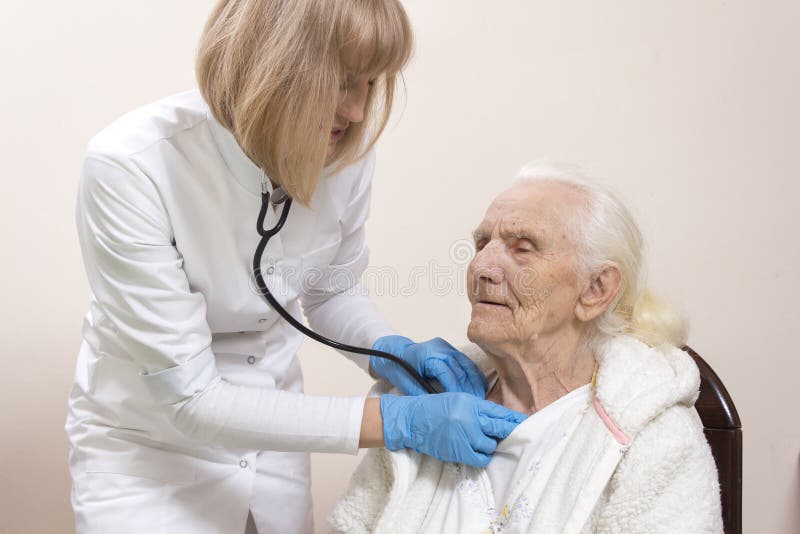 Le docteur d'interniste de femme dans un manteau blanc et des gants médicaux de laboratoire examine les poumons d'une femme grise image libre de droits