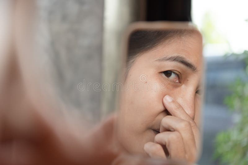 Le donne di mezza età stanno esaminando lo specchio per vedere il wr facciale fotografia stock Le donne di mezza età stanno esaminando lo specchio per vedere il wr facciale fotografia stock