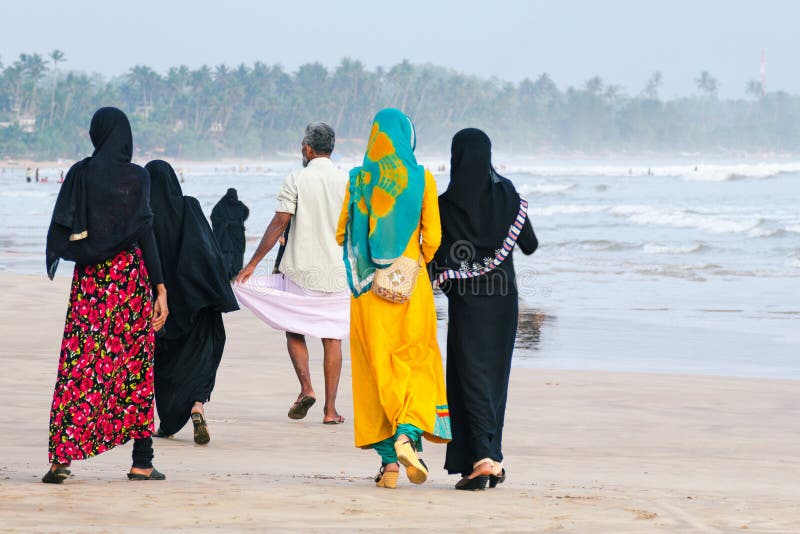 Le donne musulmane camminano lungo la spiaggia, un uomo cammina avanti fotografia stock libera da diritti Le donne musulmane camminano lungo la spiaggia, un uomo cammina avanti fotografia stock libera da diritti