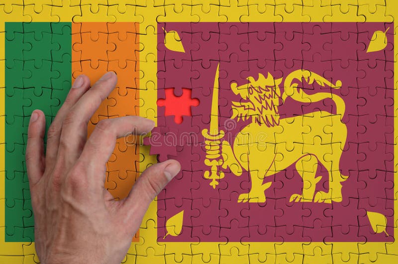 Le drapeau de Sri Lanka est dépeint sur un puzzle, que la main du ` s d'homme accomplit pour plier photographie stock libre de droits Le drapeau de Sri Lanka est dépeint sur un puzzle, que la main du ` s d'homme accomplit pour plier photographie stock libre de droits