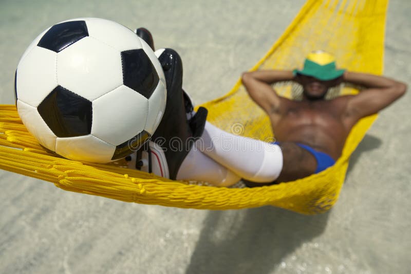 Le footballeur brésilien détend avec le football dans l'hamac de plage images stock Le footballeur brésilien détend avec le football dans l'hamac de plage images stock