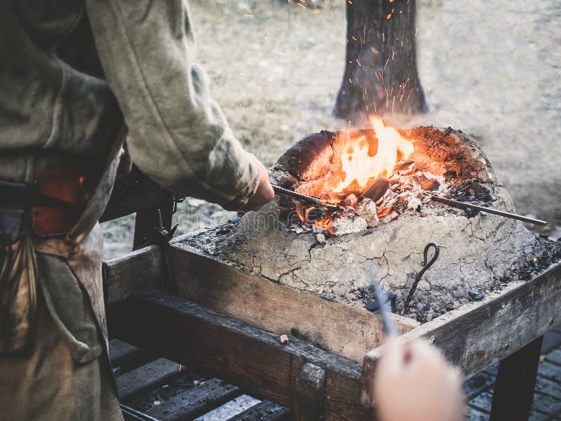 Le forgeron tient la billette au-dessus des charbons chauds dans un four d'argile fabrication de chauffage d'épée en métal de fer images libres de droits Le forgeron tient la billette au-dessus des charbons chauds dans un four d'argile fabrication de chauffage d'épée en métal de fer images libres de droits