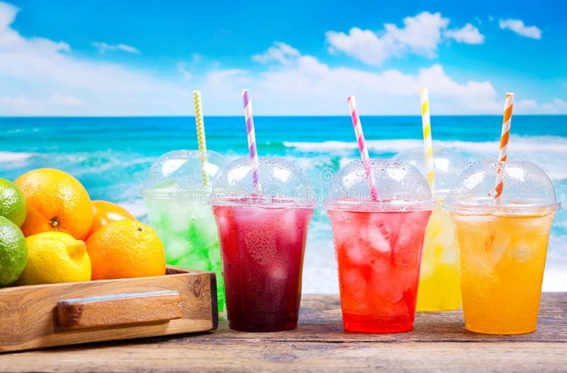 Le froid coloré boit dans des tasses en plastique sur la plage