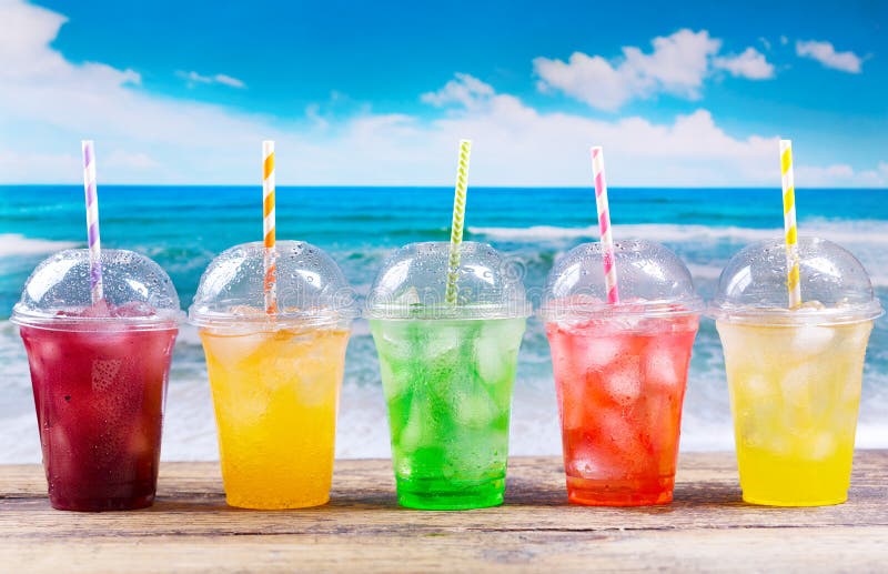 Le froid coloré boit dans des tasses en plastique sur la plage