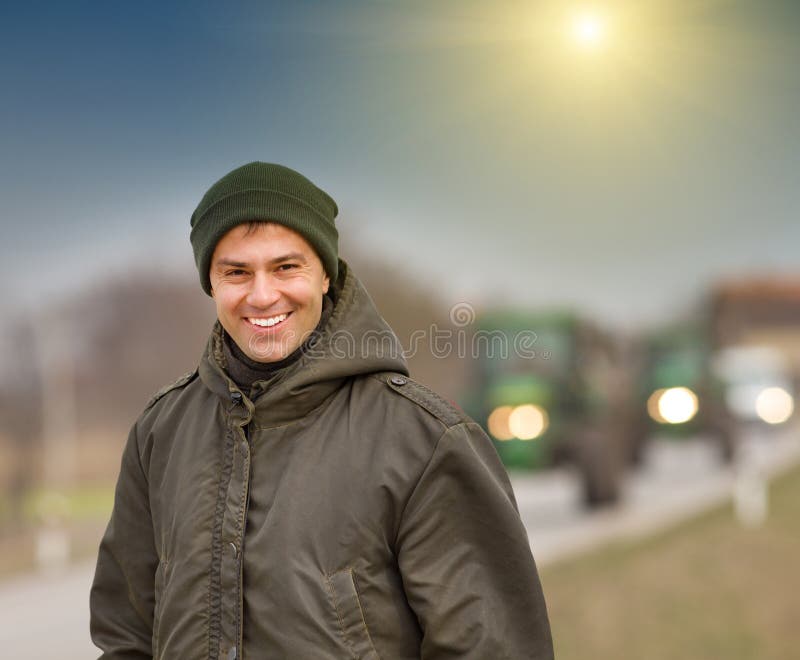 Happy farmer standing on farmland with tractors in background. Happy farmer standing on farmland with tractors in background