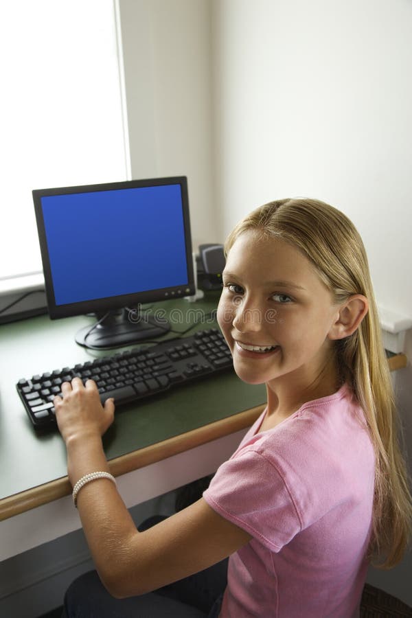 Caucasian pre-teen girl at computer looking over shoulder smiling at viewer. Caucasian pre-teen girl at computer looking over shoulder smiling at viewer.