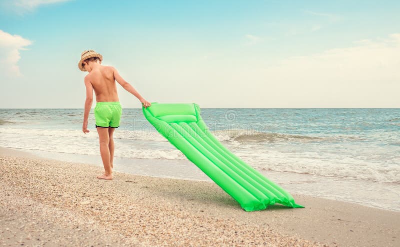 Le gar?on avec le matelas de natation marche sur la plage de mer de sable photos stock Le gar?on avec le matelas de natation marche sur la plage de mer de sable photos stock