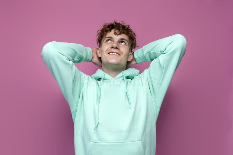Le gars curé satisfait dans le hoodie à la menthe se repose les mains derrière sa tête sur fond rose isolé photo stock