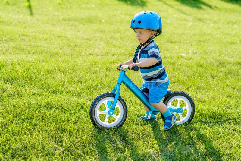 Le garçon dans le casque montant un vélo bleu d'équilibre courent le vélo images stock Le garçon dans le casque montant un vélo bleu d'équilibre courent le vélo images stock
