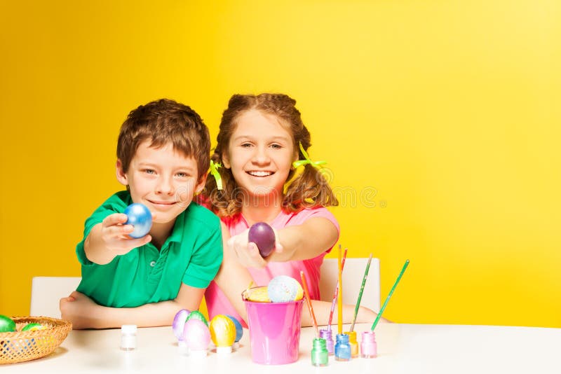 Le garçon et la fille heureux montrent des oeufs de pâques sur la table photographie stock libre de droits Le garçon et la fille heureux montrent des oeufs de pâques sur la table photographie stock libre de droits