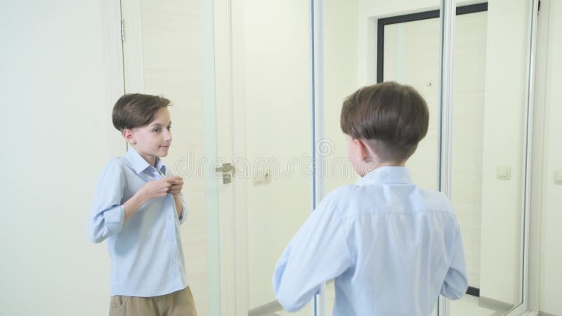 Le garçon ferme la fermeture éclair de sa chemise bleue et regarde dans le miroir.