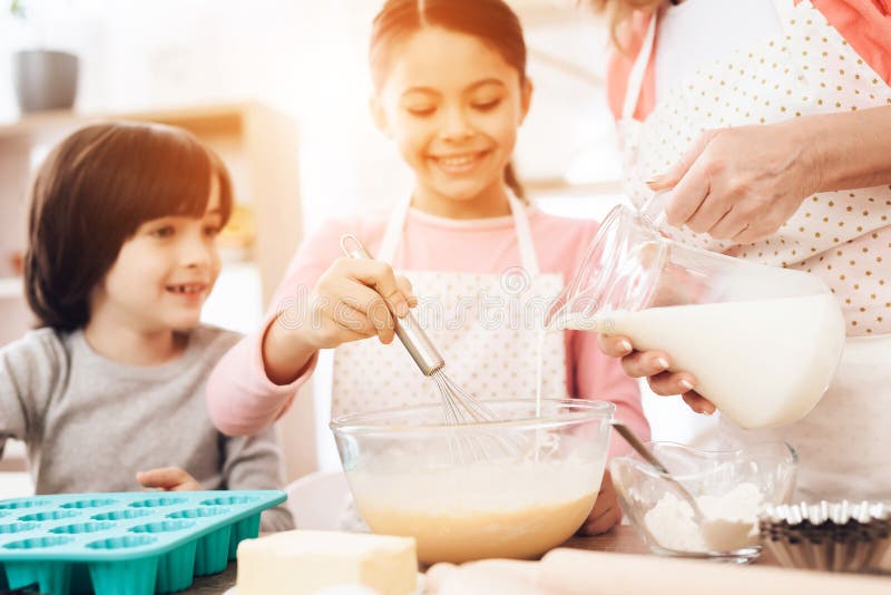Le garçon heureux regarde la petite fille qui bat des oeufs dans la cuvette, où la belle grand-mère verse le lait de la cruche photos libres de droits Le garçon heureux regarde la petite fille qui bat des oeufs dans la cuvette, où la belle grand-mère verse le lait de la cruche photos libres de droits