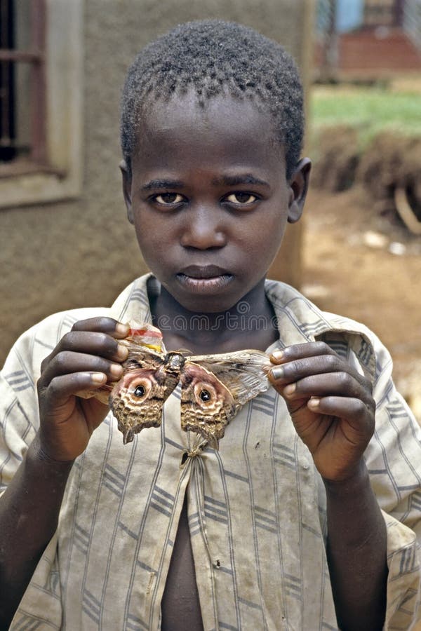 Le garçon ougandais pose fièrement avec la mite colorée photo libre de droits Le garçon ougandais pose fièrement avec la mite colorée photo libre de droits