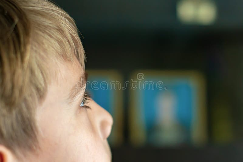 Le garçon regarde la TV, les yeux de l'enfant sont étroit, dans la perspective d'une télévision fonctionnante photographie stock Le garçon regarde la TV, les yeux de l'enfant sont étroit, dans la perspective d'une télévision fonctionnante photographie stock