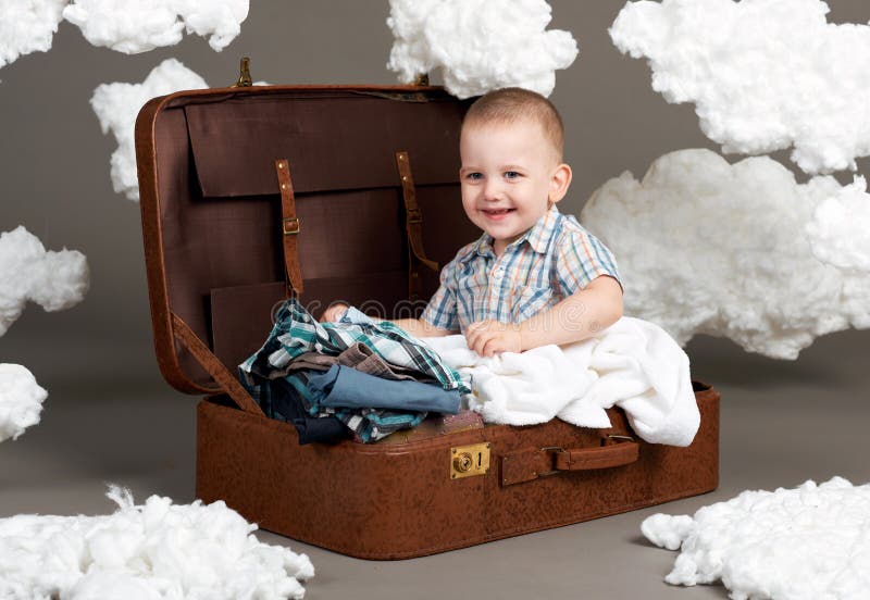 Le garçon s'assied dans une valise et part en voyage, nuages d'ouate comme décoration, fond gris photographie stock libre de droits Le garçon s'assied dans une valise et part en voyage, nuages d'ouate comme décoration, fond gris photographie stock libre de droits