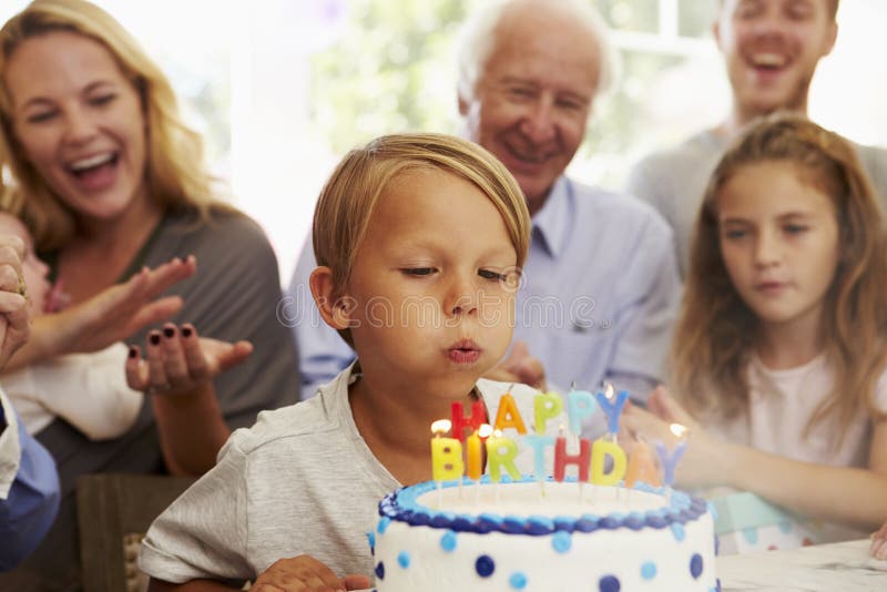 Le garçon souffle des bougies de gâteau d'anniversaire à la partie de famille image stock Le garçon souffle des bougies de gâteau d'anniversaire à la partie de famille image stock