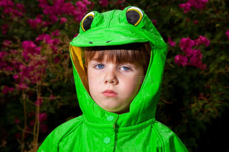Le garçon Unamused dans l'imperméable de grenouille regarde l'appareil-photo image libre de droits Le garçon Unamused dans l'imperméable de grenouille regarde l'appareil-photo image libre de droits