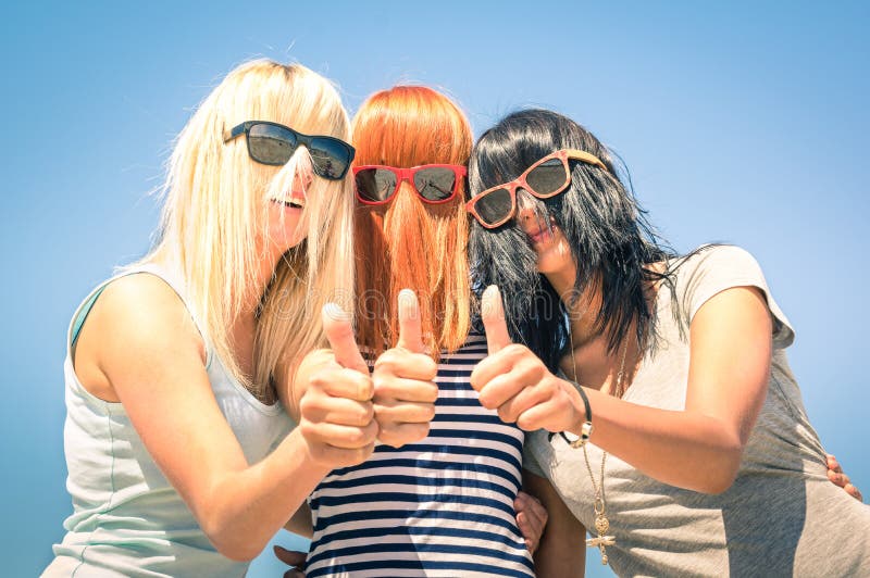 Le giovani amiche con capelli divertenti si divertono con i pollici su fotografia stock Le giovani amiche con capelli divertenti si divertono con i pollici su fotografia stock