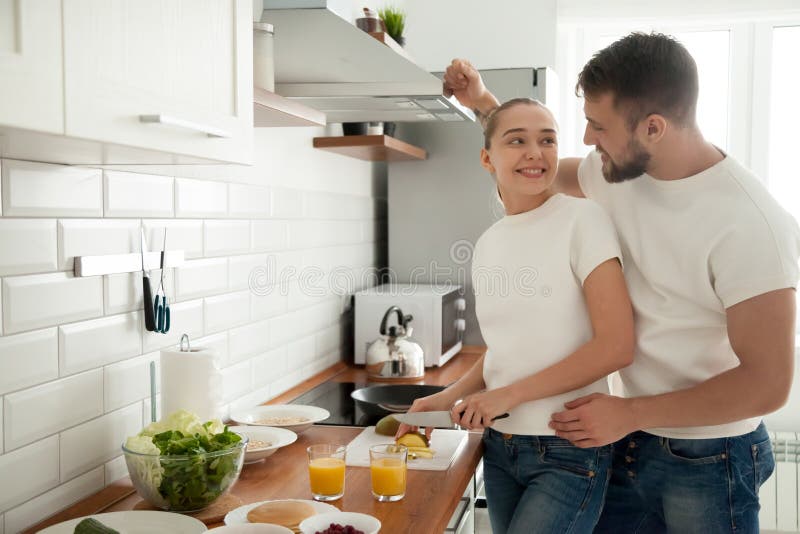 Le giovani coppie felici preparano insieme la prima colazione in cucina immagine stock libera da diritti Le giovani coppie felici preparano insieme la prima colazione in cucina immagine stock libera da diritti