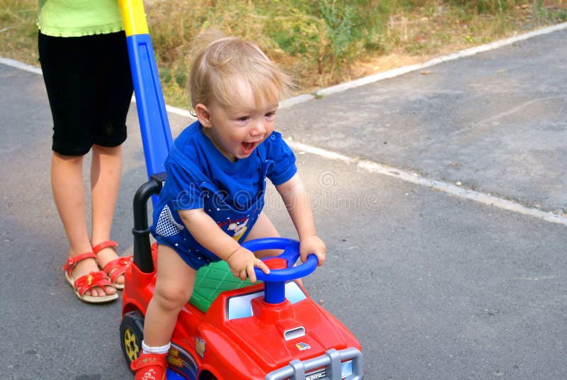 The small joyful boy goes at the wheel the red children's car. The small joyful boy goes at the wheel the red children's car