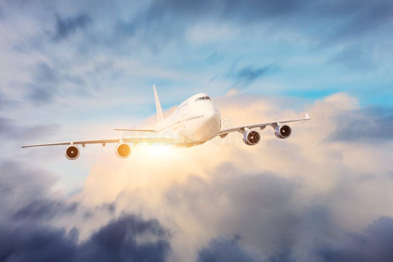 Le grand avion de transport de passagers quatre moteurs de jet vole par les nuages denses avec le soleil lumineux photo stock Le grand avion de transport de passagers quatre moteurs de jet vole par les nuages denses avec le soleil lumineux photo stock