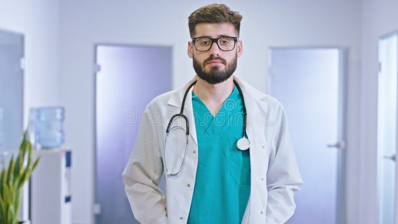 Le grand médecin de look de type dans un couloir d'hôpital moderne avec des lunettes donnant directement à la caméra l'a concentré