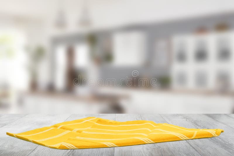 Closeup of a empty yellow striped tablecloth or napkin on a bright rustic wooden table against abstract blurred kittchen background. Template for food and product display montage. Closeup of a empty yellow striped tablecloth or napkin on a bright rustic wooden table against abstract blurred kittchen background. Template for food and product display montage
