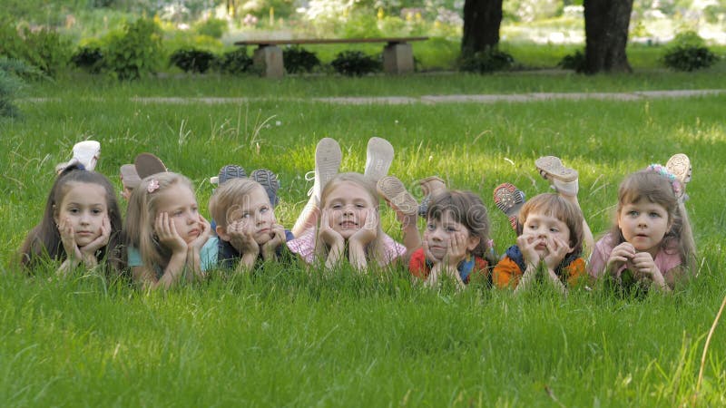 Le groupe d'enfants heureux se trouvant sur l'herbe verte dehors se garent au printemps clips vidéos