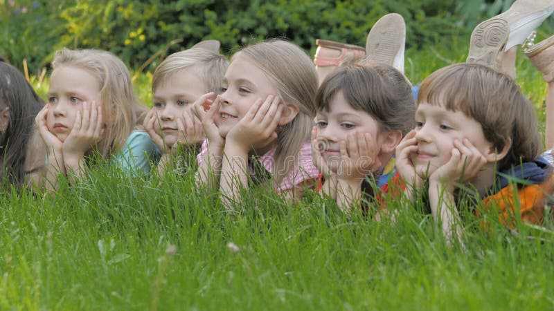 Le groupe d'enfants heureux se trouvant sur l'herbe verte dehors se garent au printemps banque de vidéos