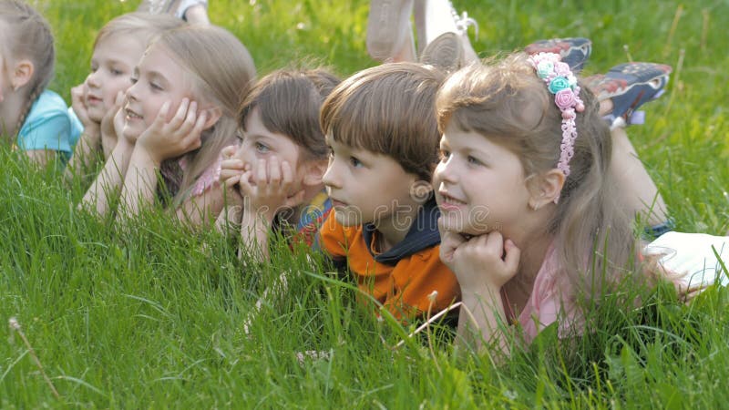 Le groupe d'enfants heureux se trouvant sur l'herbe verte dehors se garent au printemps clips vidéos