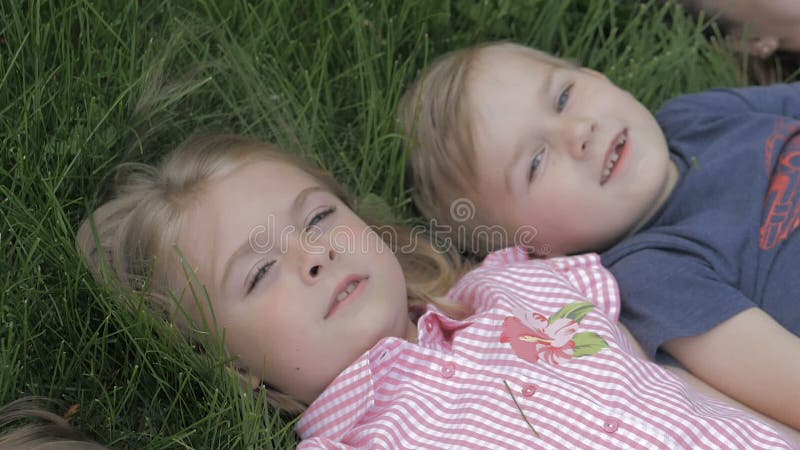 Le groupe d'enfants heureux se trouvant sur l'herbe verte dehors se garent au printemps clips vidéos