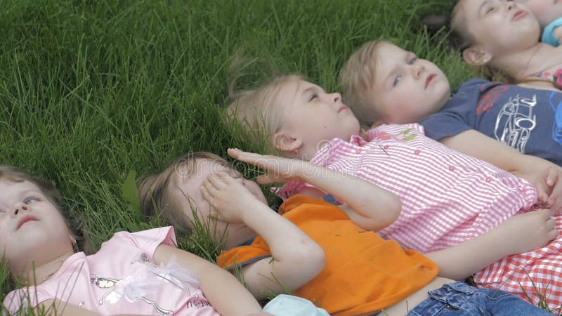 Le groupe d'enfants heureux se trouvant sur l'herbe verte dehors se garent au printemps clips vidéos