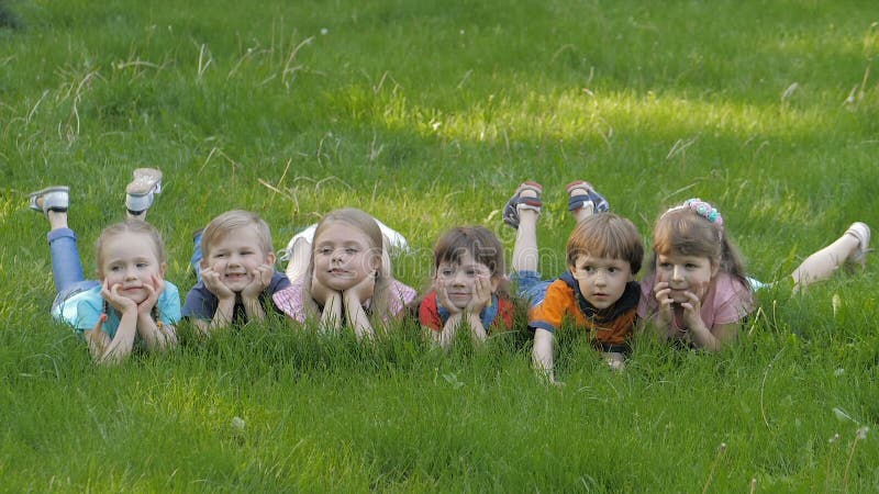 Le groupe d'enfants heureux se trouvant sur l'herbe verte dehors se garent au printemps clips vidéos