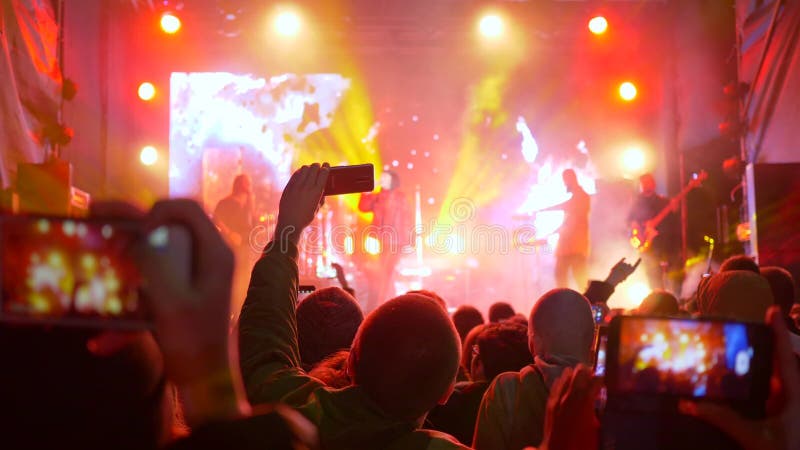 Le groupe de rock, beaucoup de mains avec le mobile font des représentations de photo sur l'étape allumée banque de vidéos