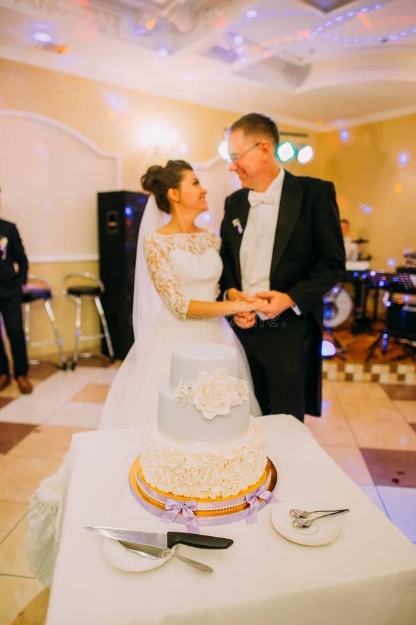 Le gâteau blanc de massepain avec des fleurs au fond des nouveaux mariés heureux images stock