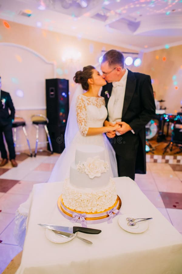 Le gâteau de mariage floral blanc au fond des couples de baiser de nouveaux mariés photographie stock libre de droits