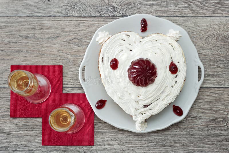 Le gâteau en forme de coeur avec le marmelade rouge et deux verres de champagne ont servi sur des serviettes sur le fond en bois image libre de droits Le gâteau en forme de coeur avec le marmelade rouge et deux verres de champagne ont servi sur des serviettes sur le fond en bois image libre de droits