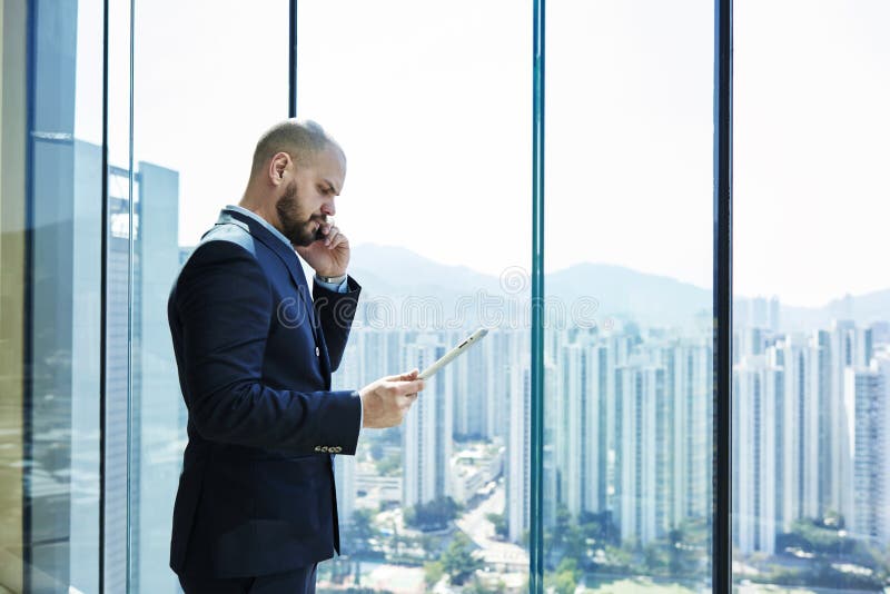 Le jeune avocat avec le visage sérieux et le comprimé numérique à disposition parle au téléphone portable avec le client photos stock Le jeune avocat avec le visage sérieux et le comprimé numérique à disposition parle au téléphone portable avec le client photos stock