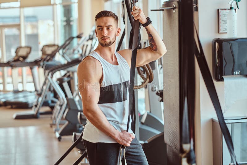 Le jeune bodybuilder attirant pose ? c?t? de l'appareil s'exer?ant au gymnase ensoleill? photos stock Le jeune bodybuilder attirant pose ? c?t? de l'appareil s'exer?ant au gymnase ensoleill? photos stock