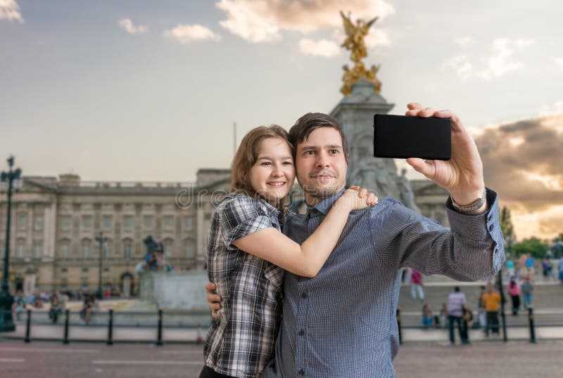 Le jeune couple heureux prend la photo de selfie près du Palais de Buckingham photo libre de droits Le jeune couple heureux prend la photo de selfie près du Palais de Buckingham photo libre de droits