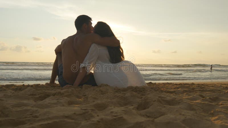 Le jeune couple romantique apprécie le beau coucher du soleil se reposant sur la plage et étreindre Une femme et un homme s'assie images stock Le jeune couple romantique apprécie le beau coucher du soleil se reposant sur la plage et étreindre Une femme et un homme s'assie images stock