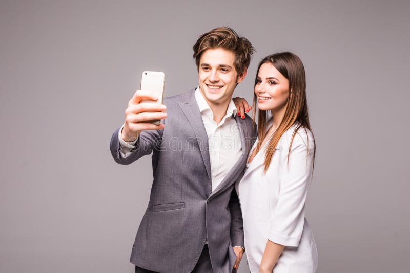 Le jeune couple utilise les téléphones intelligents et sourit tandis que debout prend le selfie sur un fond gris image libre de droits Le jeune couple utilise les téléphones intelligents et sourit tandis que debout prend le selfie sur un fond gris image libre de droits