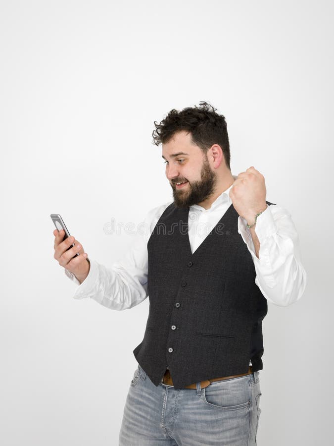 Le jeune homme avec la barbe noire est posant et regardant son smartphone devant le fond blanc avec diff?rentes ?motions photo libre de droits Le jeune homme avec la barbe noire est posant et regardant son smartphone devant le fond blanc avec diff?rentes ?motions photo libre de droits