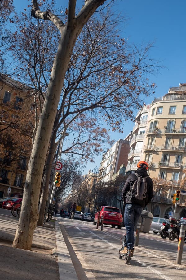 Le jeune homme avec le sac à dos monte un scooter électrique de poussée sur la route, Barcelone, Espagne image stock Le jeune homme avec le sac à dos monte un scooter électrique de poussée sur la route, Barcelone, Espagne image stock