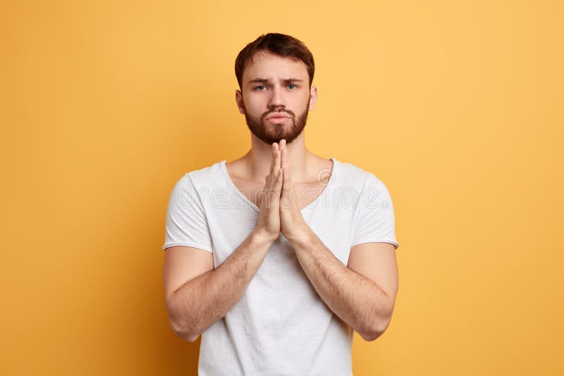 Le jeune homme beau avec parler en faveur l'expression priante, garde des paumes ensemble photo stock Le jeune homme beau avec parler en faveur l'expression priante, garde des paumes ensemble photo stock