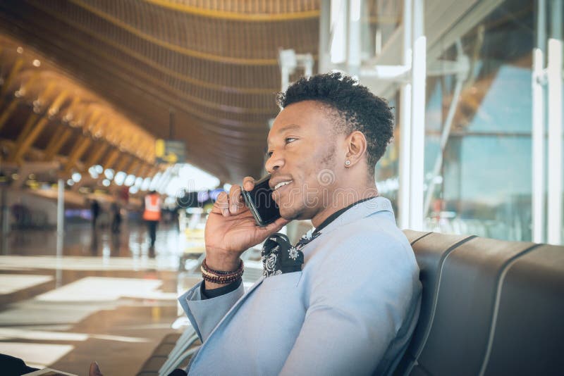 Le jeune homme d'affaires est assis dans l'aéroport souriant et parlant b image libre de droits Le jeune homme d'affaires est assis dans l'aéroport souriant et parlant b image libre de droits