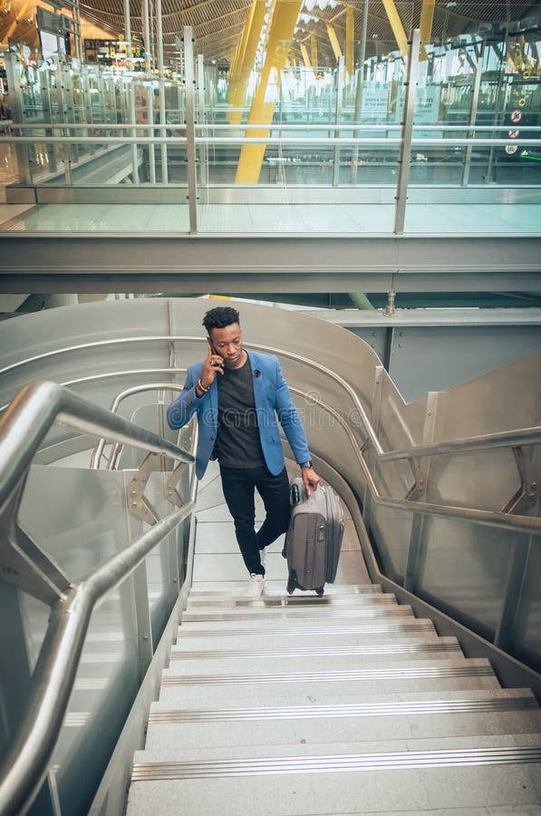 Le jeune homme d'affaires monte des escaliers dans l'aéroport parlant par t photo libre de droits Le jeune homme d'affaires monte des escaliers dans l'aéroport parlant par t photo libre de droits