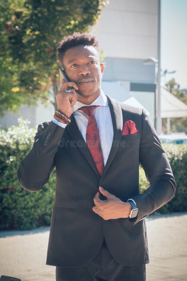 Le jeune homme d'affaires se lève en dehors de l'aéroport regardant le Th photo stock Le jeune homme d'affaires se lève en dehors de l'aéroport regardant le Th photo stock